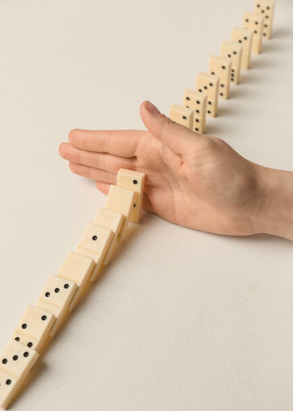 Dominosteine stoppen – Prozesse unter Kontrolle bringen Eine Hand stoppt fallende Dominosteine – Symbol für das rechtzeitige Erkennen und Stoppen ineffizienter Abläufe.
